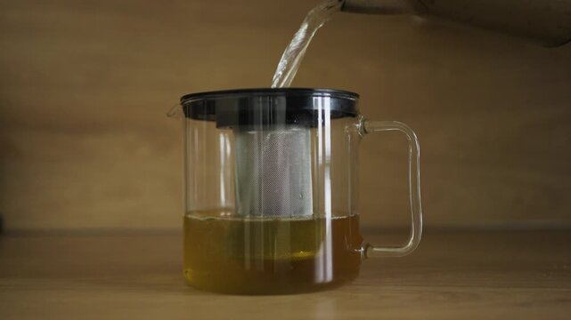 Hot water pouring into glass tea kettle with infuser, wood background