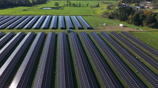 Drone footage captures rows of solar panels stretching across lush green fields in The Basin, Melbourne. Bright sunlight highlights clean energy technology in a modern, open landscape.