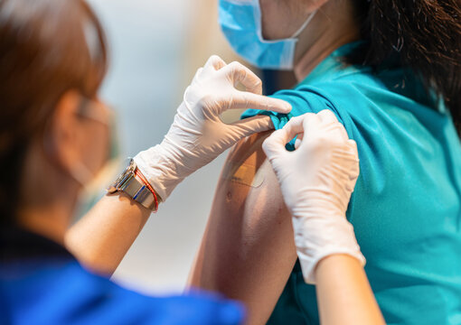 A healthcare worker in medical gloves applying an adhesive bandage plaster to a patient's upper arm following a vaccination injection.