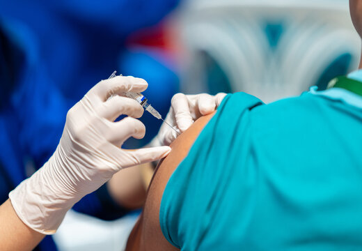 A doctor injecting a dose of medicine or vaccine with a syringe into a patient's shoulder during a routine medical immunization session.