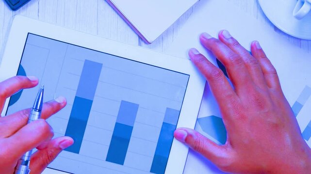 Top view of hands analyzing financial data on tablet over desk surface