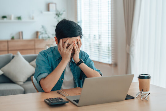 Asian man are stressed, pain in their eyes, working on laptop in living room at home