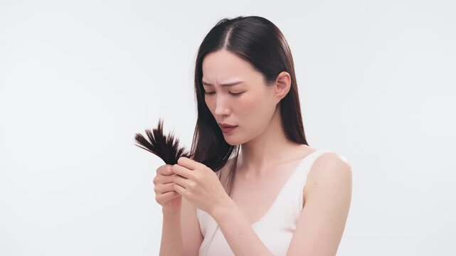 毛先の傷みや枝毛を心配そうに見つめる日本人女性（ヘアケア・悩み・ダメージ）