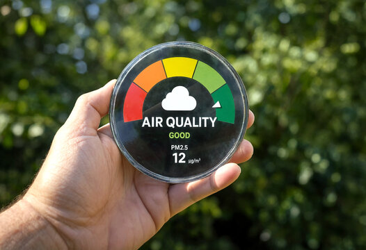 Hand holding a portable air quality monitor showing good pm25 levels outdoors with green trees