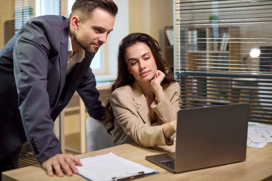 Business colleagues man woman laptop office meeting. They review finance on screen, compare report figures. Focus on analysis, budget, and planning at the desk. Financial teamwork concept.
