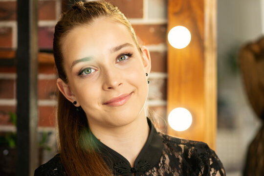 Teen Girl Smiling Near Illuminated Mirror In Beauty Salon