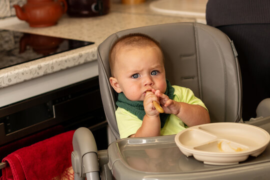 Serious Baby Boy Chews Spoon In Kitchen High Chair