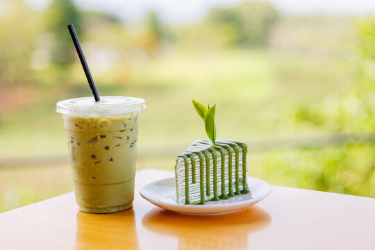 Iced matcha latte with green tea crepe cake on table for cafe menu and beverage pairing background with outdoor bokeh