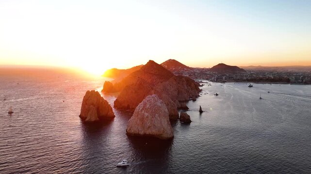 Panoramic drone shot of Land's End cliffs with vibrant sun flare at sunset in Cabo San Lucas Mexico