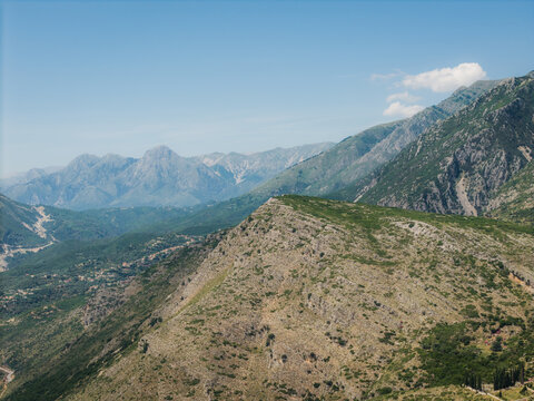 Aerial view of the rugged mountainous landscape with green slopes and rocky terrain under a clear blue sky in Qeparo Fshat, Vlore County, Albania.