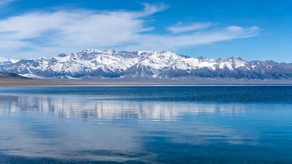 Fototapeta premium Snow Capped Mountain Range Reflected in Calm Blue Lake Under Clear Sky