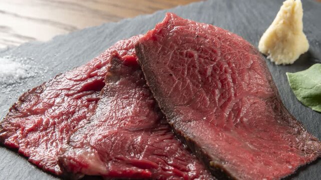 Sliced roast beef served on dark plate with cherry tomatoes garlic and arugula
