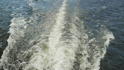 Dynamic water trail from moving vessel showing white foam textured ripples against deep blue surface. Bright daylight highlights motion fluid patterns. Ideal for travel, marine, adventure themes © VeNN