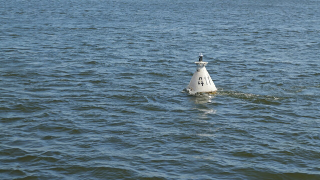 White conical buoy marked 411 floats on textured blue water under bright daylight. Calm ripples surround buoy. Composition centers buoy against open water