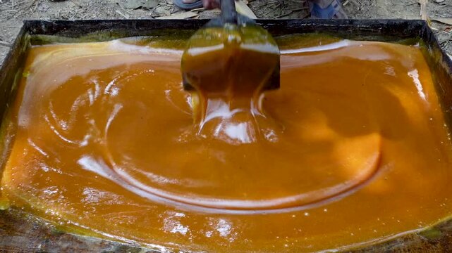 In a large rectangular pot, raw sugarcane juice is heated to a thick, red color to make jaggery.