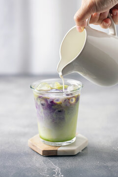 Ube tea is poured in iced matcha milk. Healthy vegan drink Ube Matcha Latte