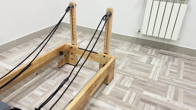Pilates reformer machine professional fitness equipment in a modern bright studio for strength training. Smooth panning shot moves across the wooden exercise apparatus.