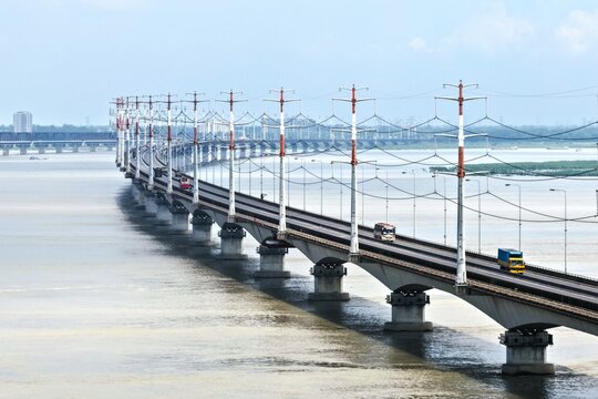 Aerial view of Jamuna Bridge spanning the wide Jamuna River with its distinctive power transmission towers, road traffic, and concrete piers in Tangail District, Dhaka Division, Bangladesh.