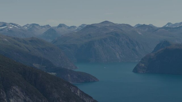 Deep blue fjord winds between tall layered fjell ridges with scattered summer snowfields in the distance.