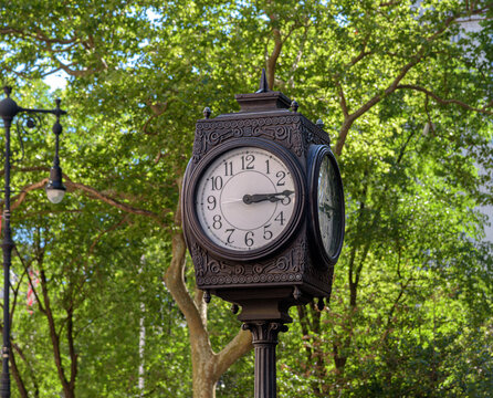 A close-up, eye-level shot captures a black, four-sided post clock with intricate ornamental metalwork framing its classic white analog faces. The clock hands indicate it is nearly quarter past three.