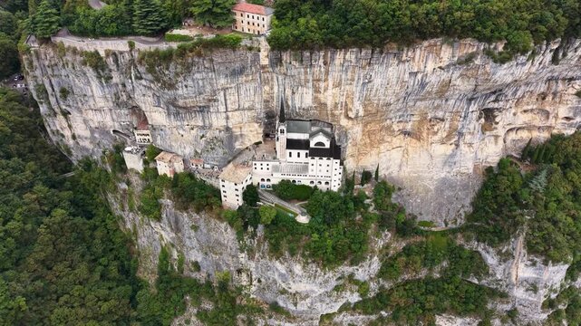 Drone view of Santuario Madonna della Corona nestled beneath towering limestone cliffs in northern Italy