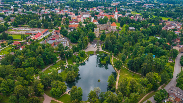 Aerial view of Cesis Castle surrounded by lush parkland, a tranquil pond, and historic town buildings in Cesis, Cesis Municipality, Latvia.