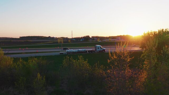 Aerial footage of a loaded commercial flatbed truck experiencing a breakdown, parked near an exit ramp along the rural I-39 corridor at dusk. Delayed delivery concept.