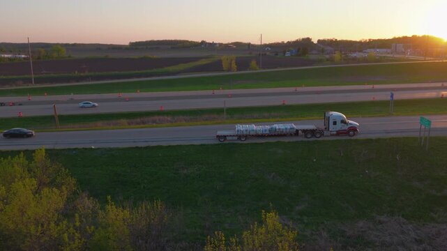 Elevated aerial clip showing a stalled flatbed truck carrying wrapped cargo parked on the shoulder ramp of the highway during sunset in Wisconsin.