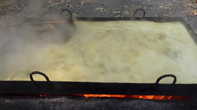 In a large rectangular pot, raw sugarcane juice is heated to a thick, red color to make jaggery.