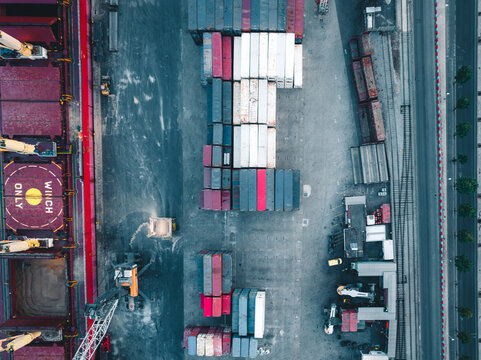 Aerial view of a busy container terminal with rows of colorful shipping containers, a large cargo ship, and industrial cranes operating on the site in Lisbon, Lisbon, Portugal.
