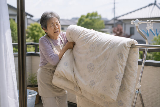 重い布団を干すのに苦労する高齢女性
