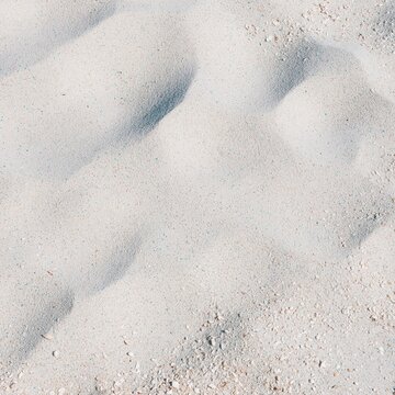 Wind-swept beach sand texture with crushed shell grit and sun-bleached ripples for coastal summer backgrounds and vacation design