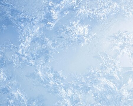 Frozen window glass with intricate ice crystals and hoar frost textures in a cool blue winter scene for seasonal backgrounds and holiday designs