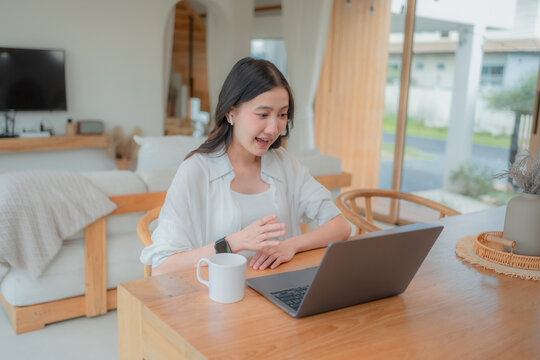 Excited Asian woman gesturing during a video call on her laptop at home, celebrating good news in an online meeting.