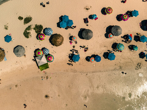 Aerial view of Balandra beach with colorful umbrellas scattered across the sand and people relaxing by the turquoise water in La Paz, Baja California Sur, Mexico.