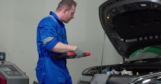 Mechanic using tester to check electric vehicle EV battery voltage under open hood in garage