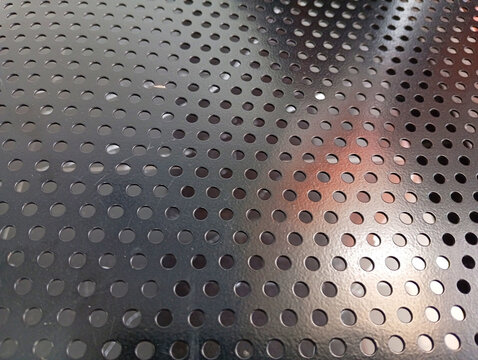 Perforated dark metal sheet texture with regular pattern of small round holes perforated material industrial