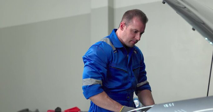 Mechanic using tester to check electric vehicle EV battery voltage under open hood in garage