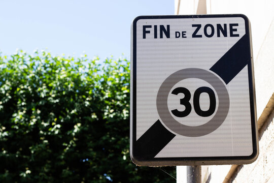 Traffic sign indicating end of speed limit zone with a maximum speed of 30 km/h, positioned against a backdrop of green foliage and a clear blue sky