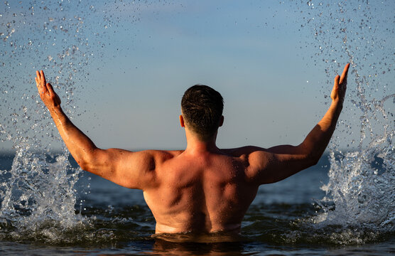 Back swimmer moves through sea waves. Back physique shows strong vitality outdoors. Wet muscular back reflects summer wellness. Natural splashes frame back and freedom.