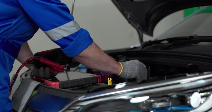 Mechanic using tester to check electric vehicle EV battery voltage under open hood in garage