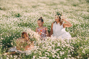 Summer picnic features mother and daughter blowing bubbles amidst blooming Bellis perennis flowers in a sunlit meadow © svetograph