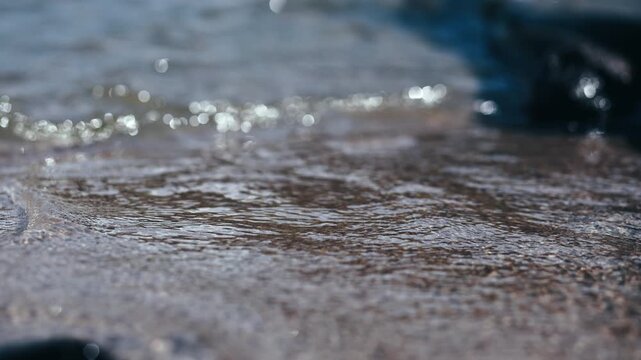 Ocean wave washing over a sandy beach as sparkling water advances and recedes along the shoreline, illustrating coastal nature and seaside movement