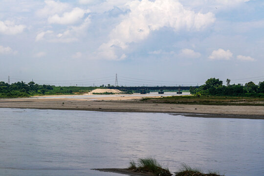 Wide River Landscape with Sandbank and Distant Railway Bridge Under Cloudy Sky