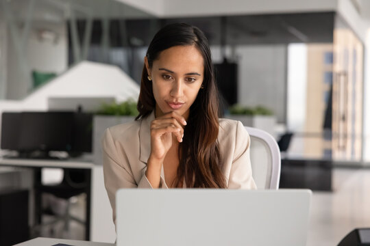 Focused businesswoman working on project, reviewing digital data on laptop screen, analyzing, thinking on strategic business decisions, sit at workplace desk in corporate office. Technology, workflow