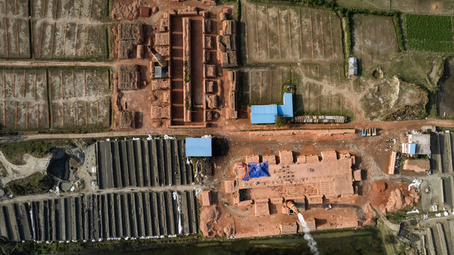 Aerial view of a brickfield with rows of drying bricks, smoking chimneys, and blue-roofed structures in the rural landscape of Chattogram, Chittagong Division, Bangladesh.