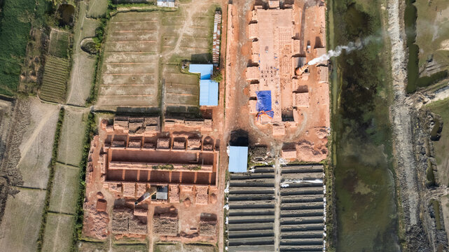 Aerial view of a brickfield with smoking chimneys, rows of drying bricks, and surrounding agricultural fields in Chattogram, Chittagong Division, Bangladesh.