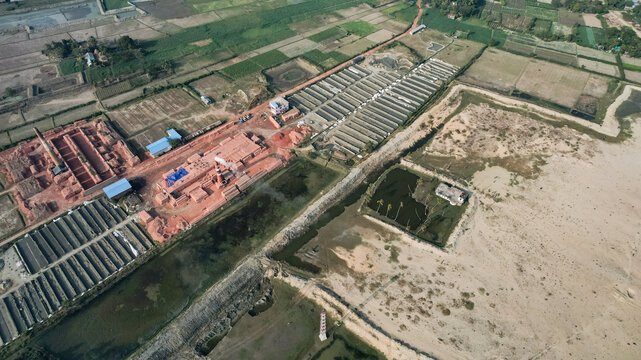 Aerial view of a brickfield with rows of drying bricks, industrial kilns, and smoke stacks surrounded by agricultural fields in Chattogram, Chittagong Division, Bangladesh.