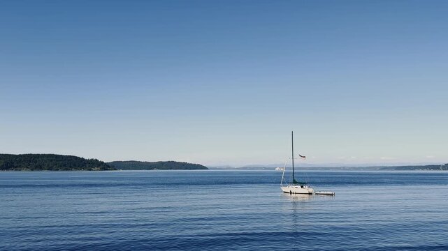 Beautiful nature with Sailboat anchored on calm blue water with a small dinghy and American flag. Scenic maritime landscape on a clear day.