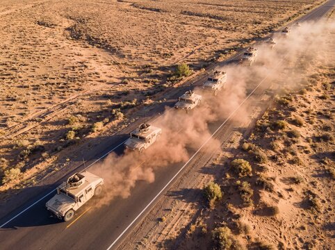 Aerial Drone View of Military Convoy of Armored Vehicles Driving on Desert Highway Kicking Up Dust